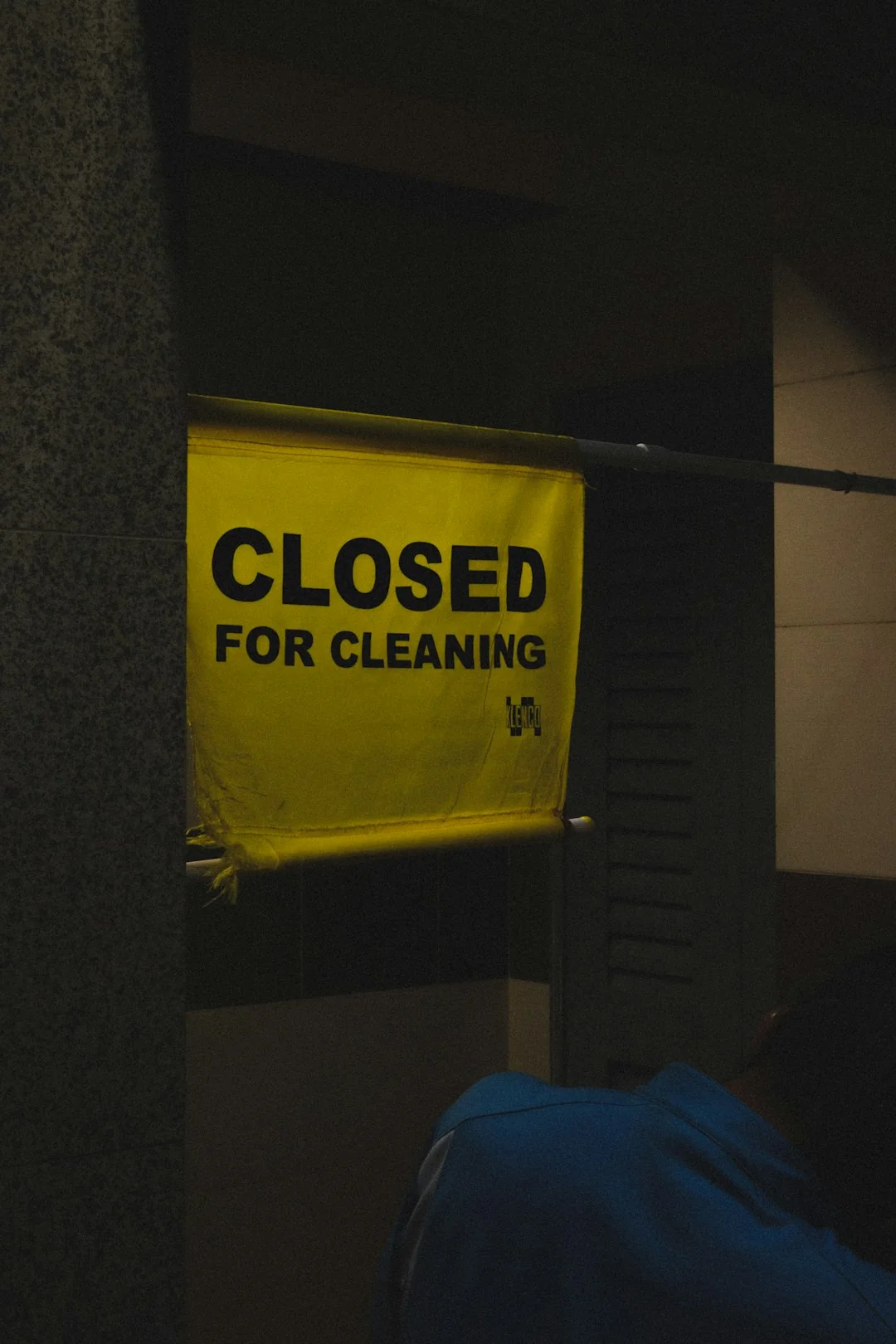 Unrecognizable bearded male wearing yellow latex gloves wiping mirror with napkin in bathroom at home